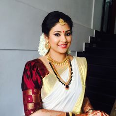 a woman in a white and red sari with gold jewelry on her neck posing for the camera