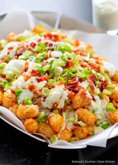 a white plate topped with tater tots covered in bacon and green onions next to a glass of milk