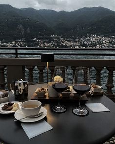 a table with two glasses of wine and plates of food on it overlooking the water