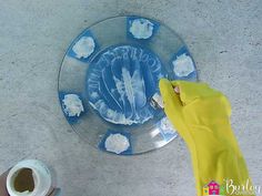 a person in yellow rubber gloves painting a plate with blue clouds on it and a cup of coffee next to it