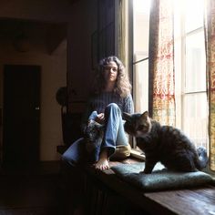 a woman sitting on a window sill next to a cat