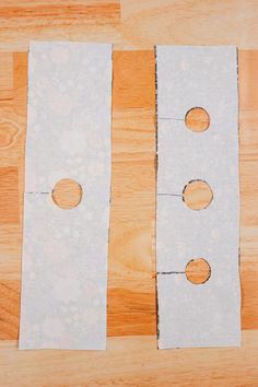 two pieces of white paper with holes cut in half on a wooden table next to a pair of scissors