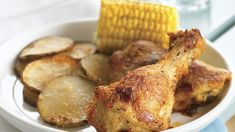 a white bowl filled with fried chicken and potatoes next to corn on the cob