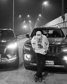 a man standing next to two parked cars on a road at night with street lights in the background