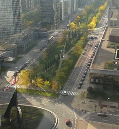 an aerial view of a city street with cars driving on the road and tall buildings in the background