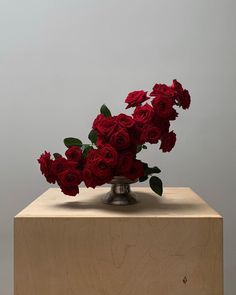 a vase filled with red roses sitting on top of a wooden block