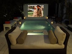 an outdoor movie theater with couches and chairs around the pool area at night time