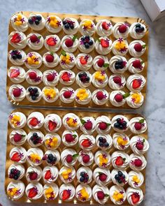 two trays filled with cupcakes covered in white frosting and topped with fruit