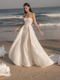 a woman standing on top of a beach next to the ocean wearing a wedding dress