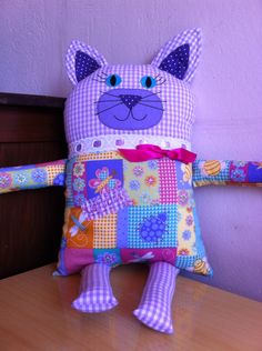 a stuffed cat sitting on top of a wooden table next to a purple and white wall