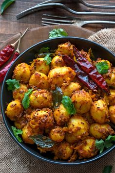 a bowl filled with potatoes and peppers on top of a wooden table next to utensils