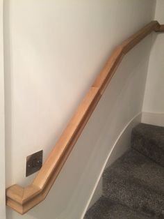 a wooden hand rail on the side of a white wall next to a gray carpeted staircase