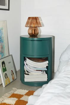 a green nightstand with magazines on it next to a lamp and other items in the corner