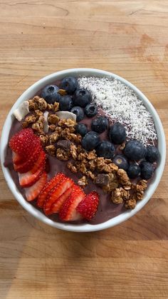 a bowl filled with granola, strawberries and blueberries on top of a wooden table