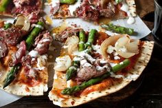 a pizza with asparagus, meat and cheese on it sitting on a table