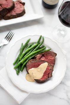 a plate with steak, green beans and gravy next to a glass of wine