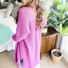 a woman standing in front of a bed wearing a pink cardigan sweater and jeans