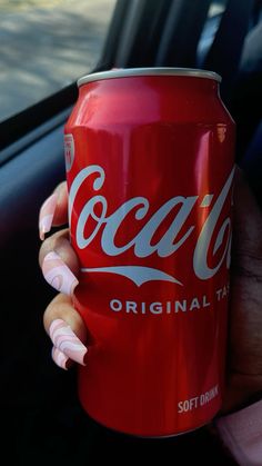 a woman holding a can of coca - cola in her hand while sitting in a car