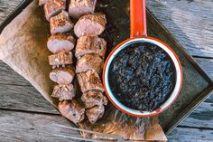 meat skewers with black sauce on a tray next to a bowl of ketchup