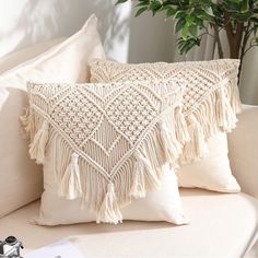 two white pillows with tassels sit on a couch next to a potted plant