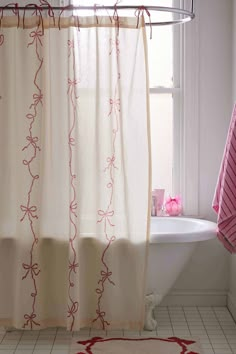 a white bath tub sitting under a window next to a shower curtain and pink rug