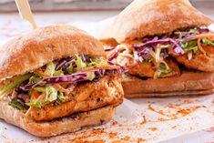 two chicken sandwiches with lettuce and coleslaw on them sitting on top of a piece of parchment paper