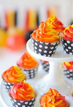 cupcakes with orange and yellow frosting on a white cake plate in front of other cupcakes