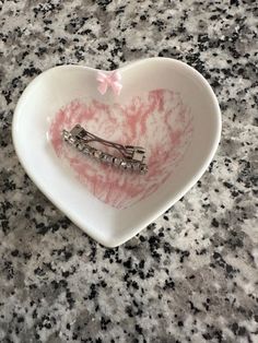 a heart shaped bowl with hair clips in it on a granite countertop next to a pink bow