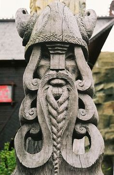 a wooden statue with an intricate design on it's face and head, in front of a building