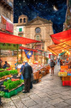 an outdoor market with lots of produce and people walking around it under the stars in the sky