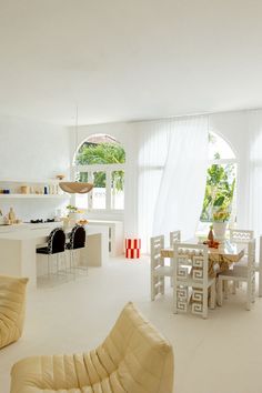 a living room filled with white furniture and lots of window sill space next to a kitchen