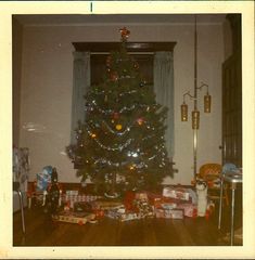 a christmas tree in the corner of a room with presents on the floor next to it