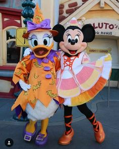 two mickey and minnie mouse characters posing for a photo in front of pluto's halloween costume shop