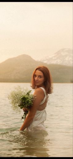 a woman standing in the water holding flowers