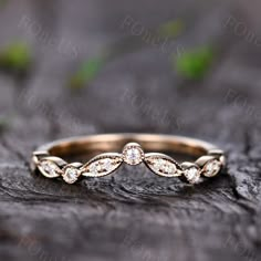 a gold wedding band with white diamonds on top of a piece of wood in the woods