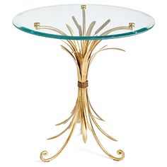 a round glass table with gold leaves on the base and a metal frame around it