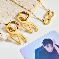 These bold gold-tone pieces include elegant hoop earrings with an abstract infinity symbol, a matching necklace with a pendant echoing the same shape, and chic mini studs for a more subtle look.  Perfect for fans and fashion-forward individuals, these pieces effortlessly combine modern design with a nod to Jung Kook's iconic style, making them ideal for both casual and formal occasions. * Dimensions - Necklace Pendant: 10 x 28 mm | 0.4'' x 1.1'' Chain: 450 mm | 17.7'' - Hoop Earrings Hoop Diamet Gifts For Bts Army, Jungkook Golden, Army Gifts, Golden Necklace, Mini Studs, Golden Jewelry, Golden Earrings, Bts Merch, Infinity Symbol