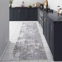 a kitchen area with black cabinets and white tile flooring, along with a gray runner rug