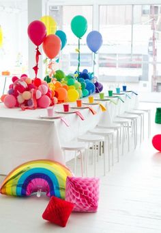 colorful balloons and streamers are on the tables at a party with white tablecloths