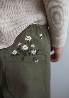 the back of a woman's pants with daisies embroidered on it and bees in the pocket