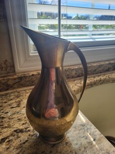 a metal pitcher sitting on top of a counter next to a window