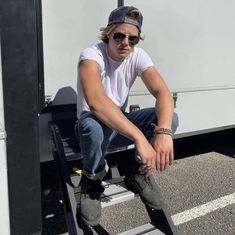 a man sitting on top of a metal step ladder next to a white trailer truck