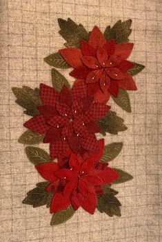 two red poinsettia flowers with green leaves on a beige background, one is embroidered onto the fabric