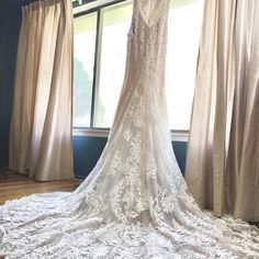 the back of a wedding dress hanging on a window sill in front of curtains