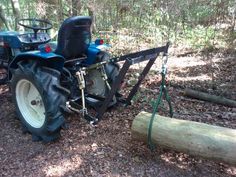 a blue tractor parked in the woods next to a tree log and some logs on the ground