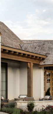 a white house with a wooden roof and pillars in front of the door is surrounded by greenery