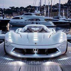 a white sports car parked on top of a wooden dock next to boats in the water