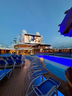 chairs are lined up on the deck of a cruise ship at night with an outdoor movie screen in the background