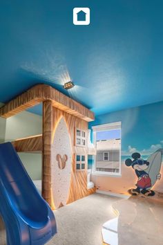 a room with a slide and mickey mouse mural on the wall