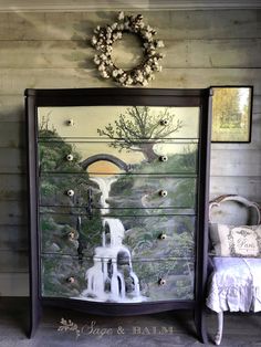 a dresser with a painting on it next to a bed